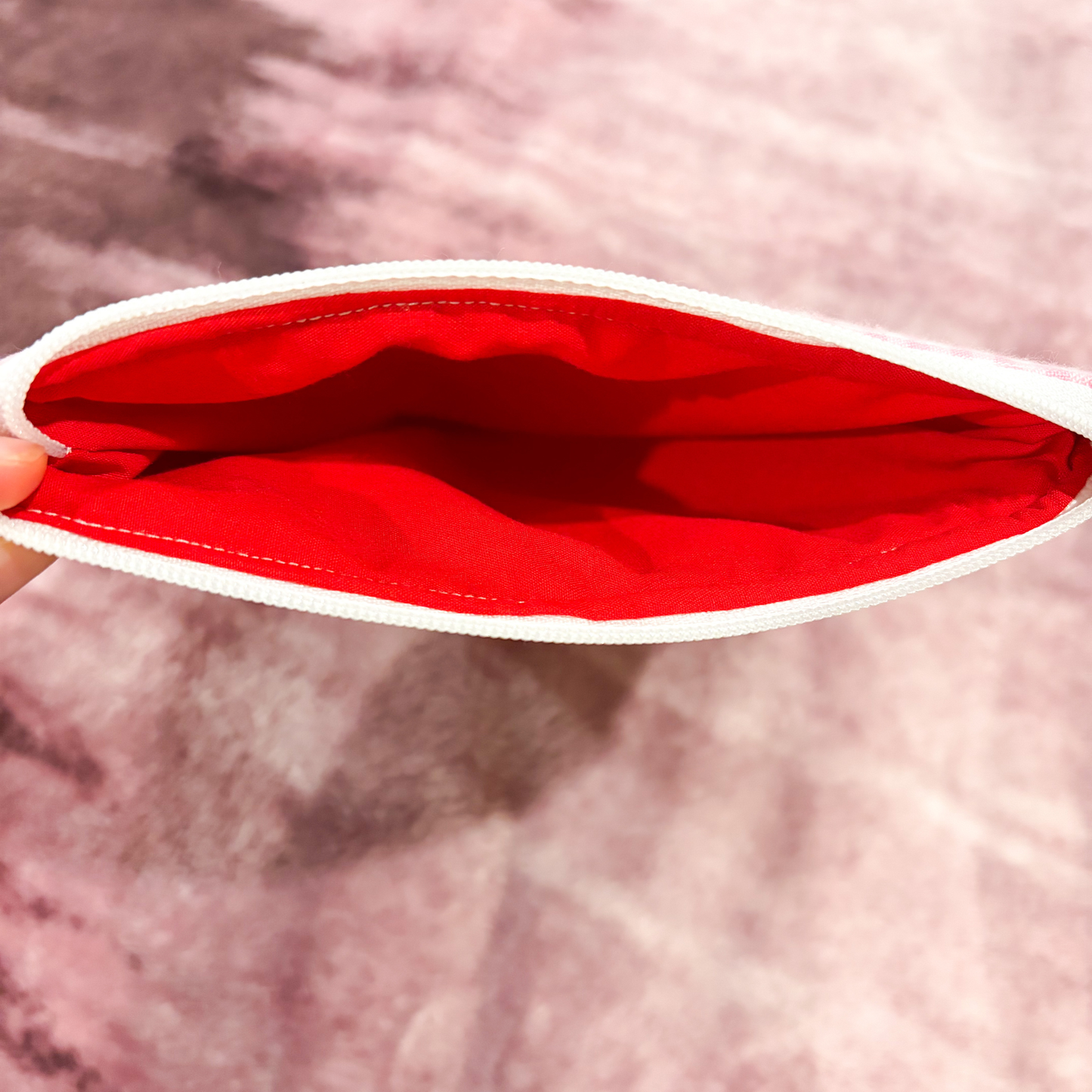 Red pouch with white rim held open against a pink background
