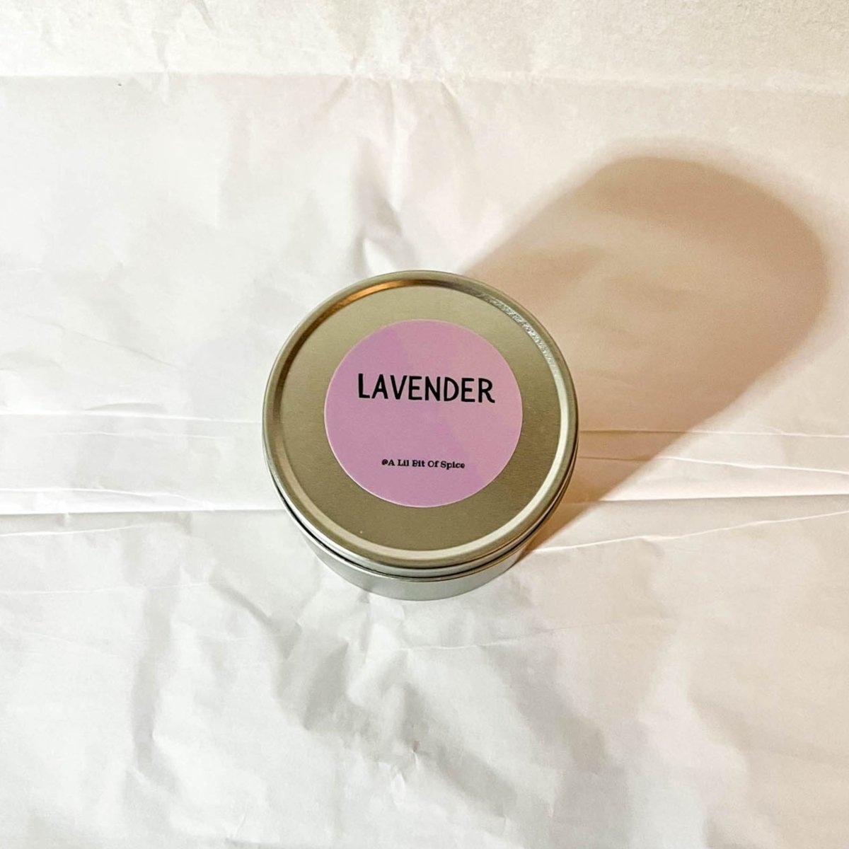 A silver candle tin labeled Lavender against a white background with a shadow