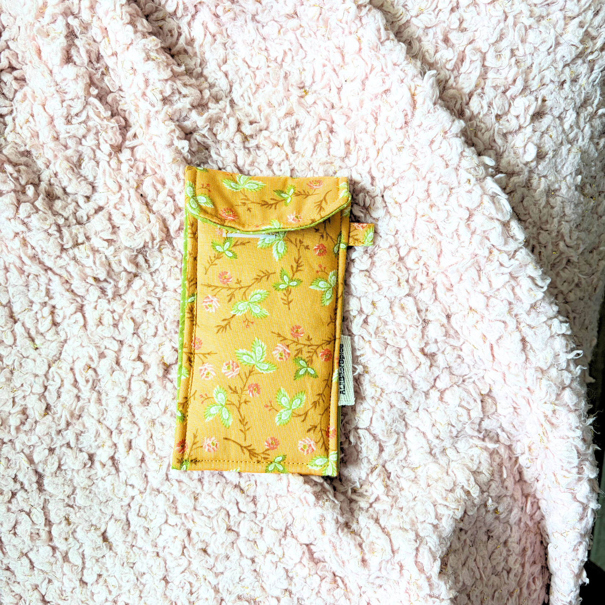 An orange fabric pouch with a green and dark orange floral pattern, placed on a textured cream sherpa blanket.