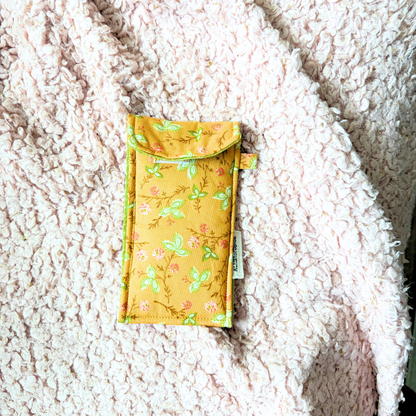 An orange fabric pouch with a green and dark orange floral pattern, placed on a textured cream sherpa blanket.