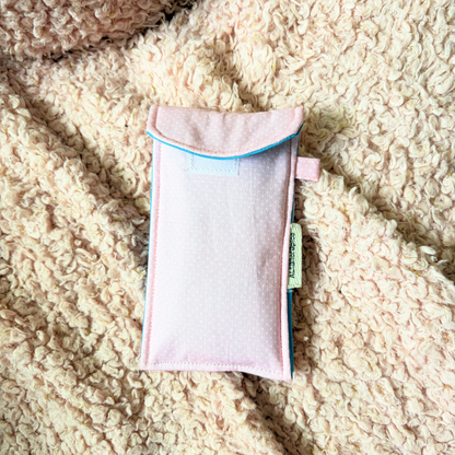 A light pink fabric pouch  placed on a textured beige sherpa blanket. A small fabric tag is visible on the side.