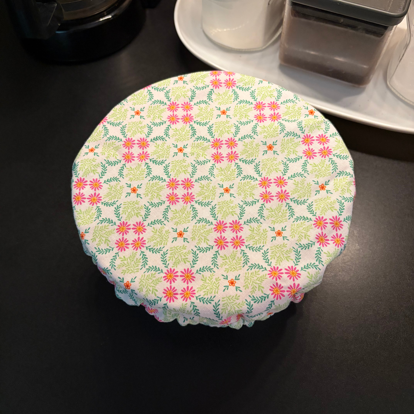 A round fabric-covered container with a colorful floral and geometric pattern, resting on a dark countertop.