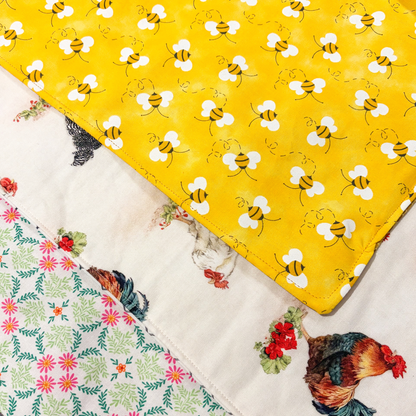 Close-up of three fabric sliding mats with bright yellow bee pattern, a floral pattern, and a rooster and chicken pattern.