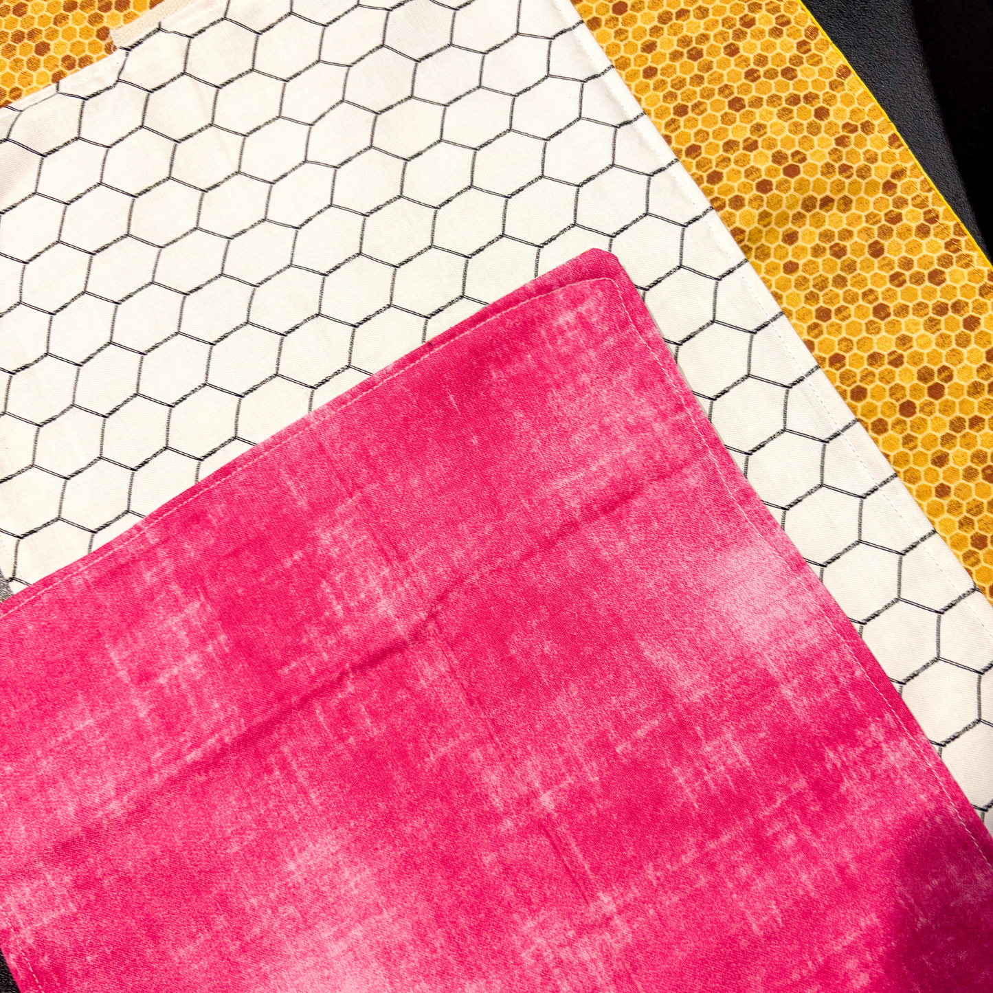 A close up of a bright pink sliding mat laid diagonally over a patterned sliding mat featuring a white hexagon grid and one with a yellow honeycomb design.