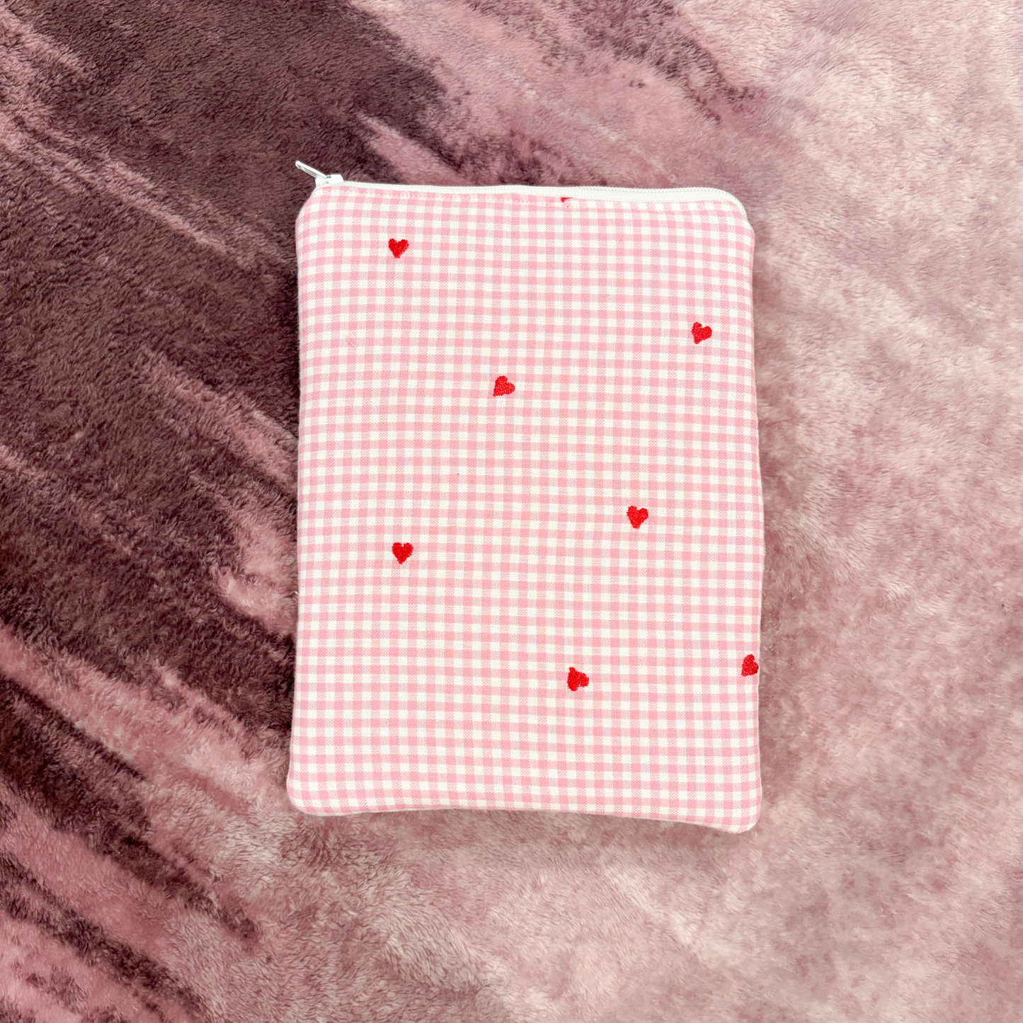 Pink gingham pouch with red hearts on a textured pink surface