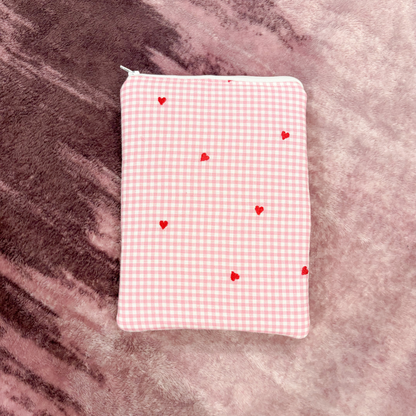 Pink gingham pouch with red hearts on a textured pink surface