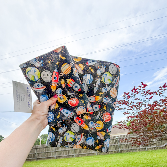 Two colorful book sleeves with space-themed designs held by a person outdoors.