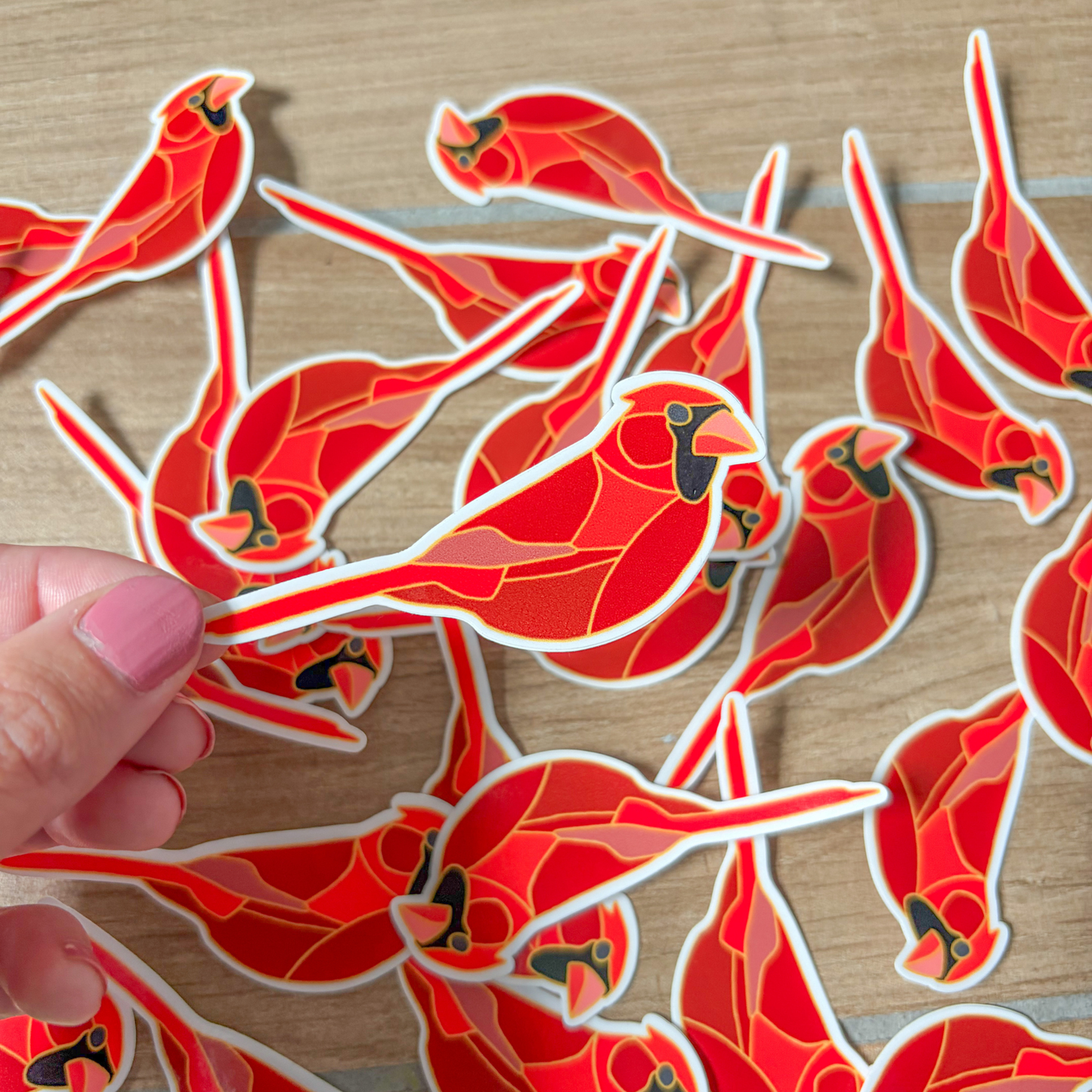 Red bird-shaped stickers on a wooden surface with a hand holding one of them.