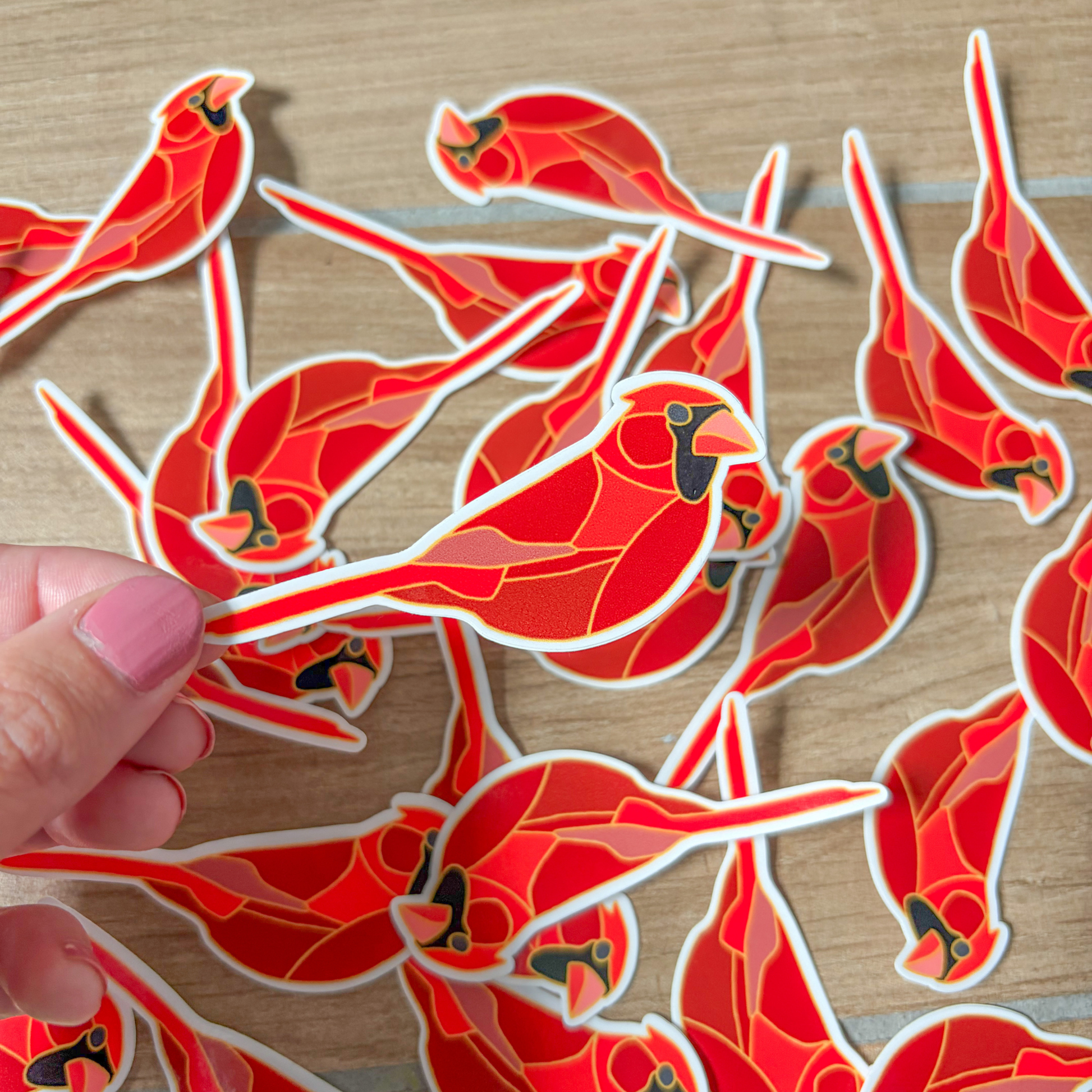 Red bird-shaped stickers on a wooden surface with a hand holding one of them.