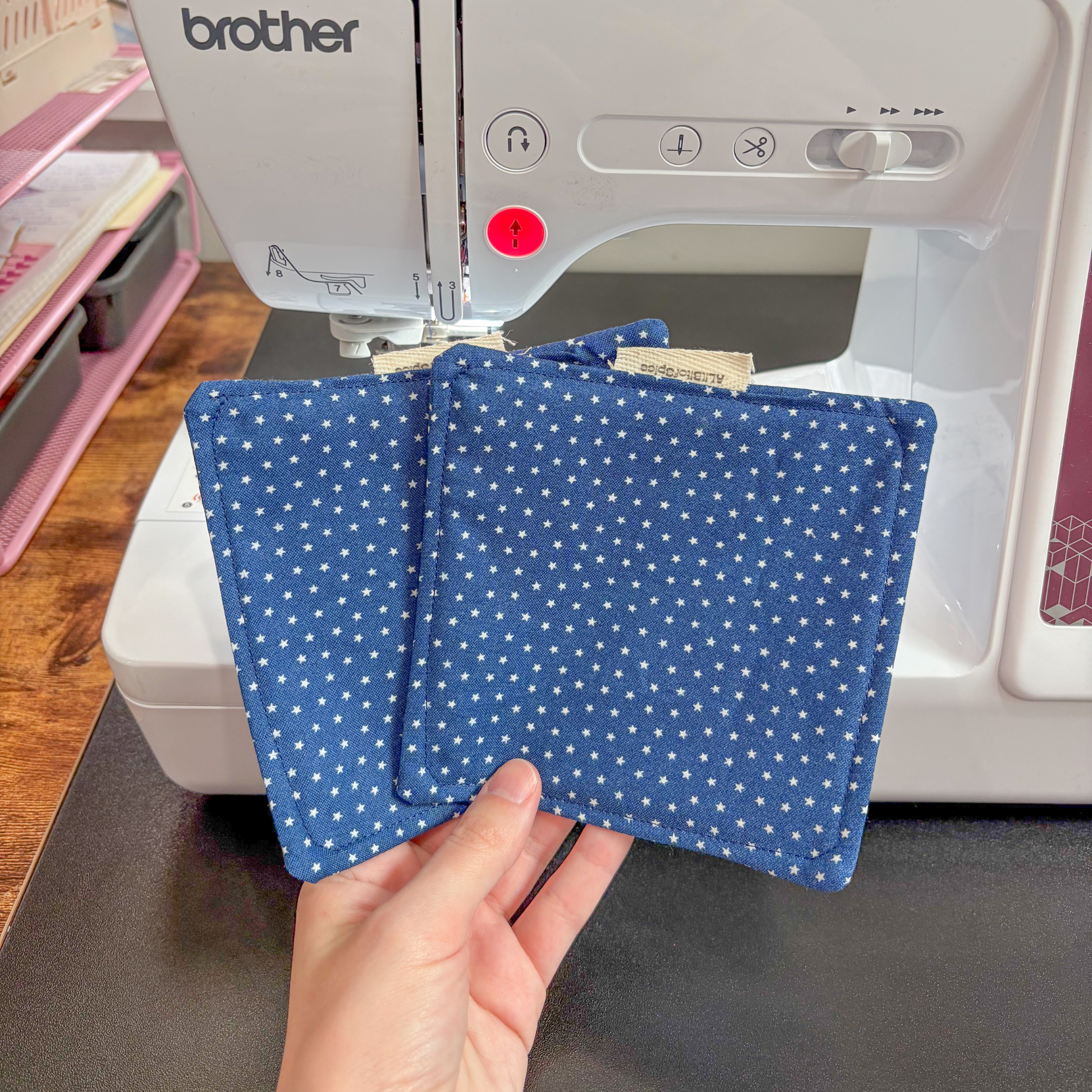Two blue star flat coasters held in front of a Brother sewing machine.
