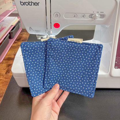 Two blue star flat coasters held in front of a Brother sewing machine.