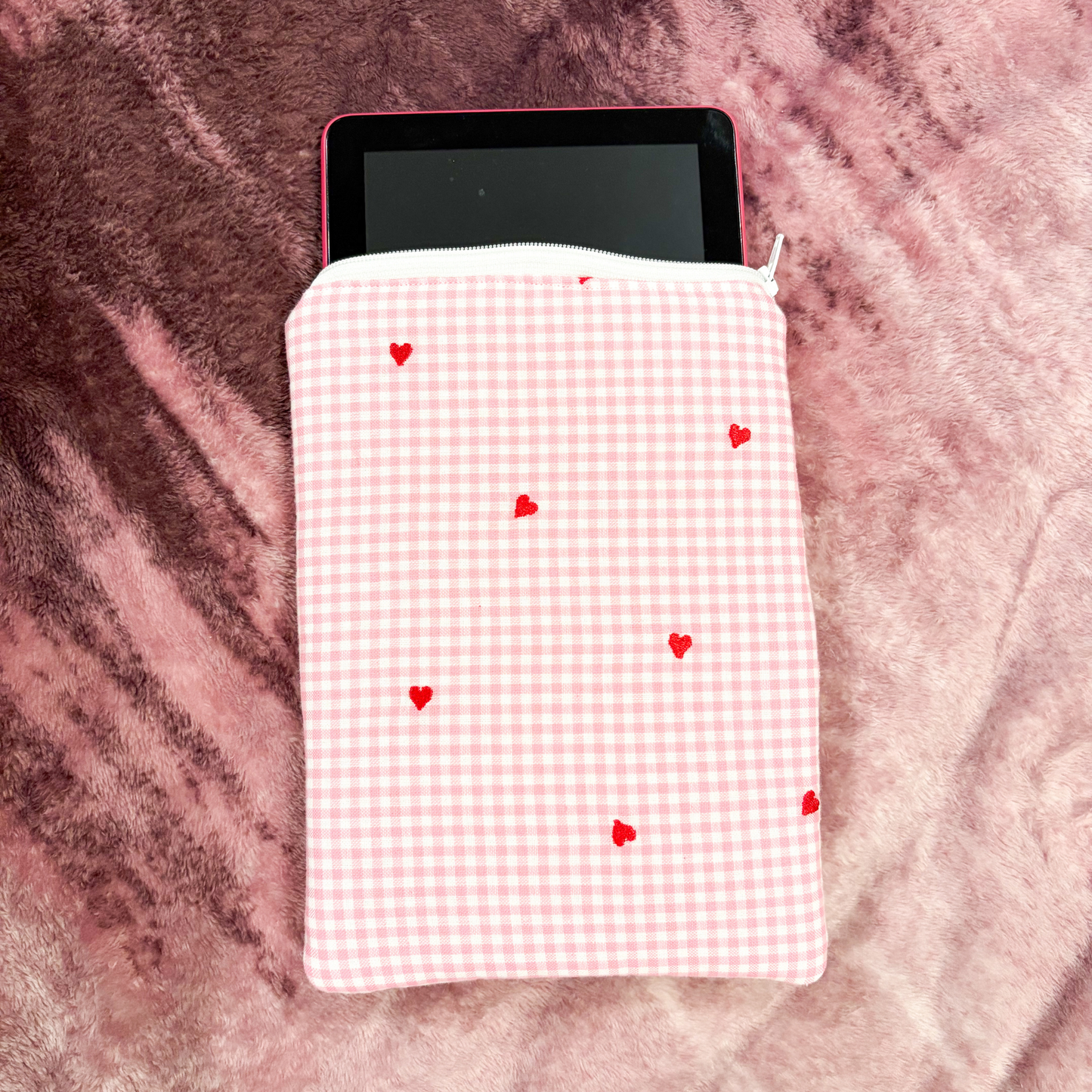 Pink gingham tablet sleeve with red hearts on a pink textured surface