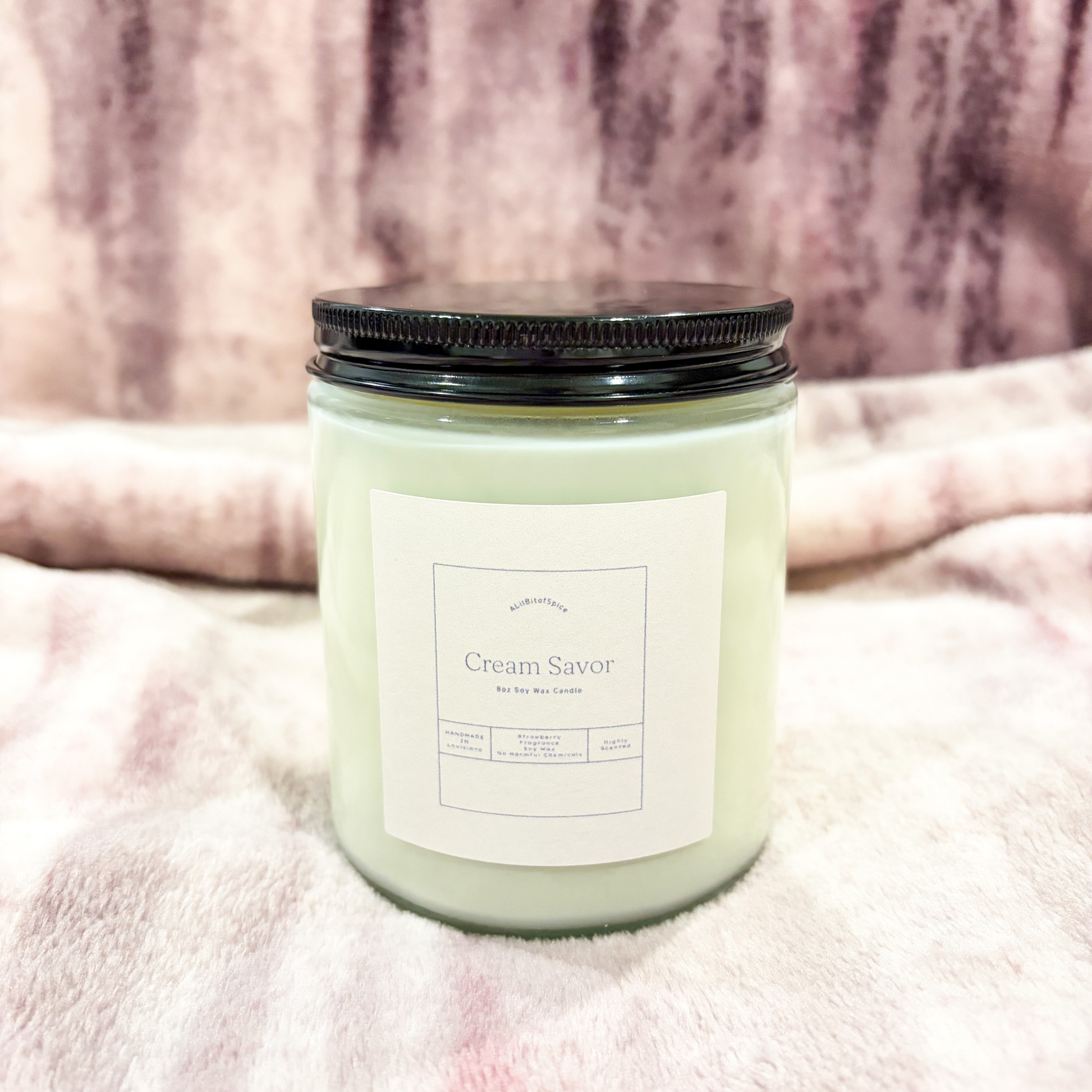 Candle labeled 'Cream Savor' on a soft pink fabric background