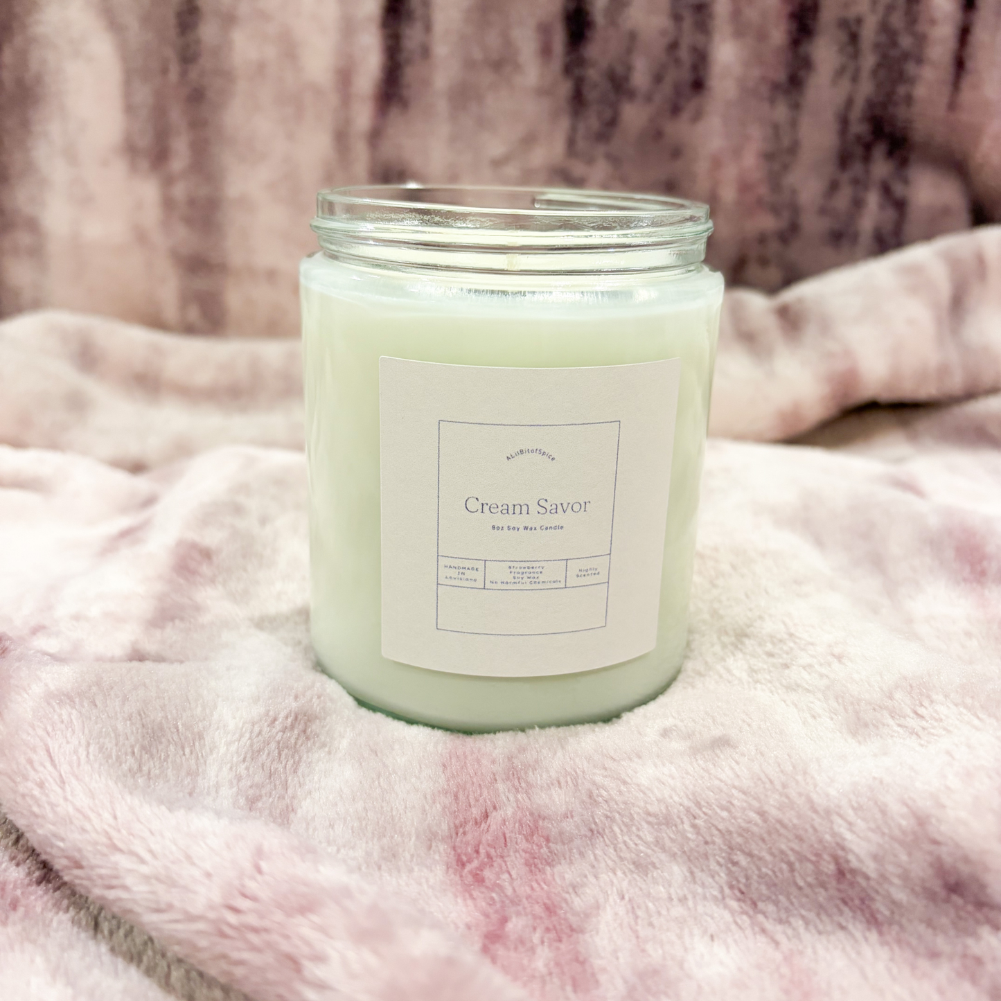 Candle labeled 'Cream Savor' on a soft pink fabric background