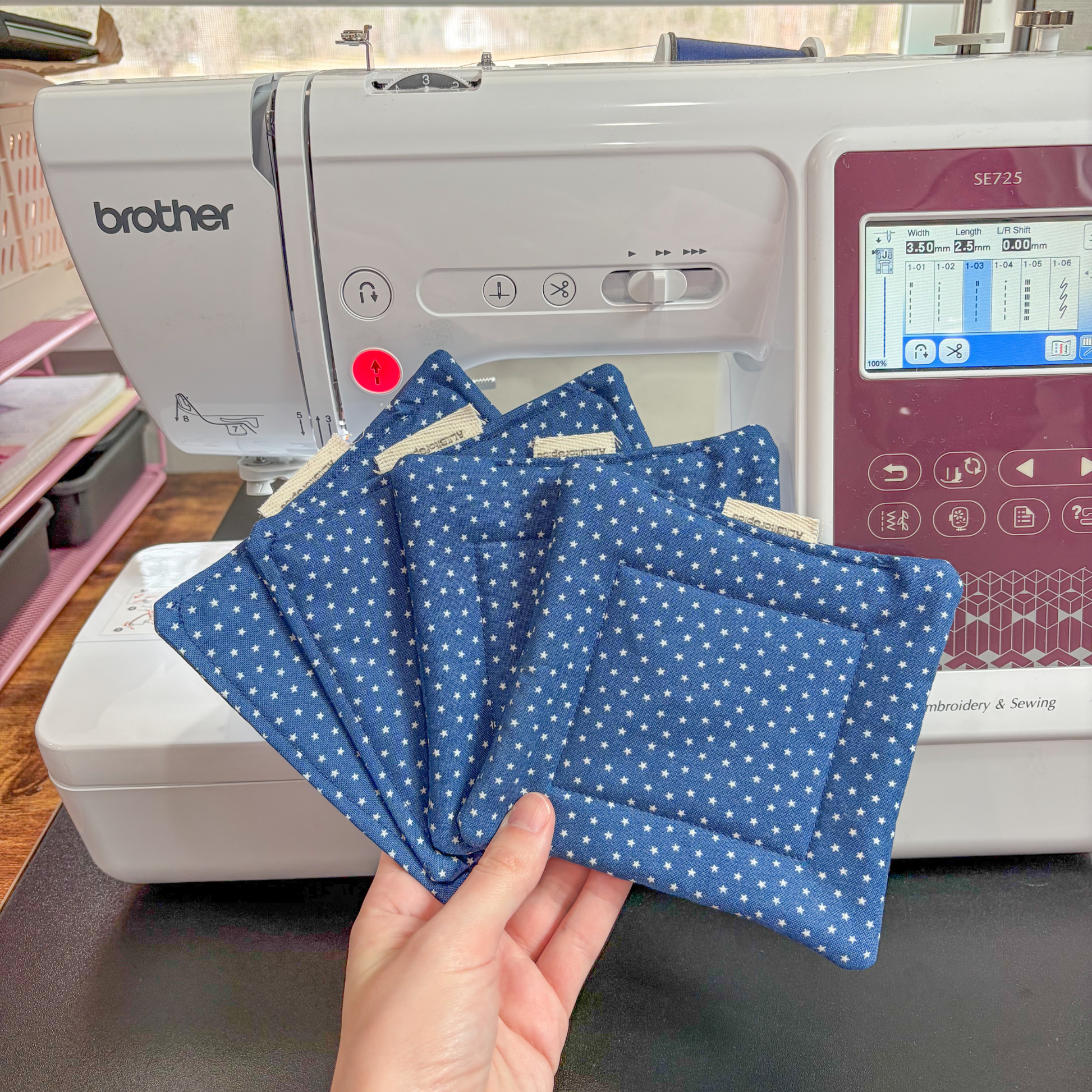 Hand holding blue polka star fabric coasters in front of a Brother sewing machine.