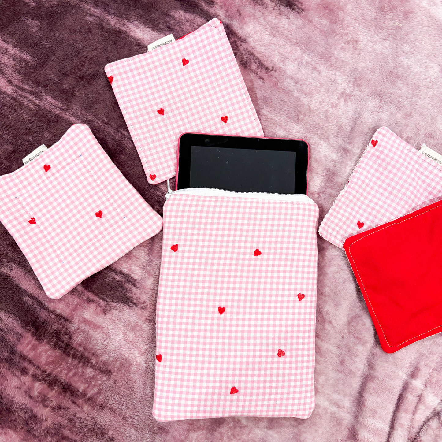 Tablet with pink checkered book sleeve featuring red hearts on a purple surface