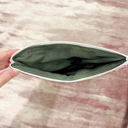 Open green pouch held by a hand on a textured pink surface