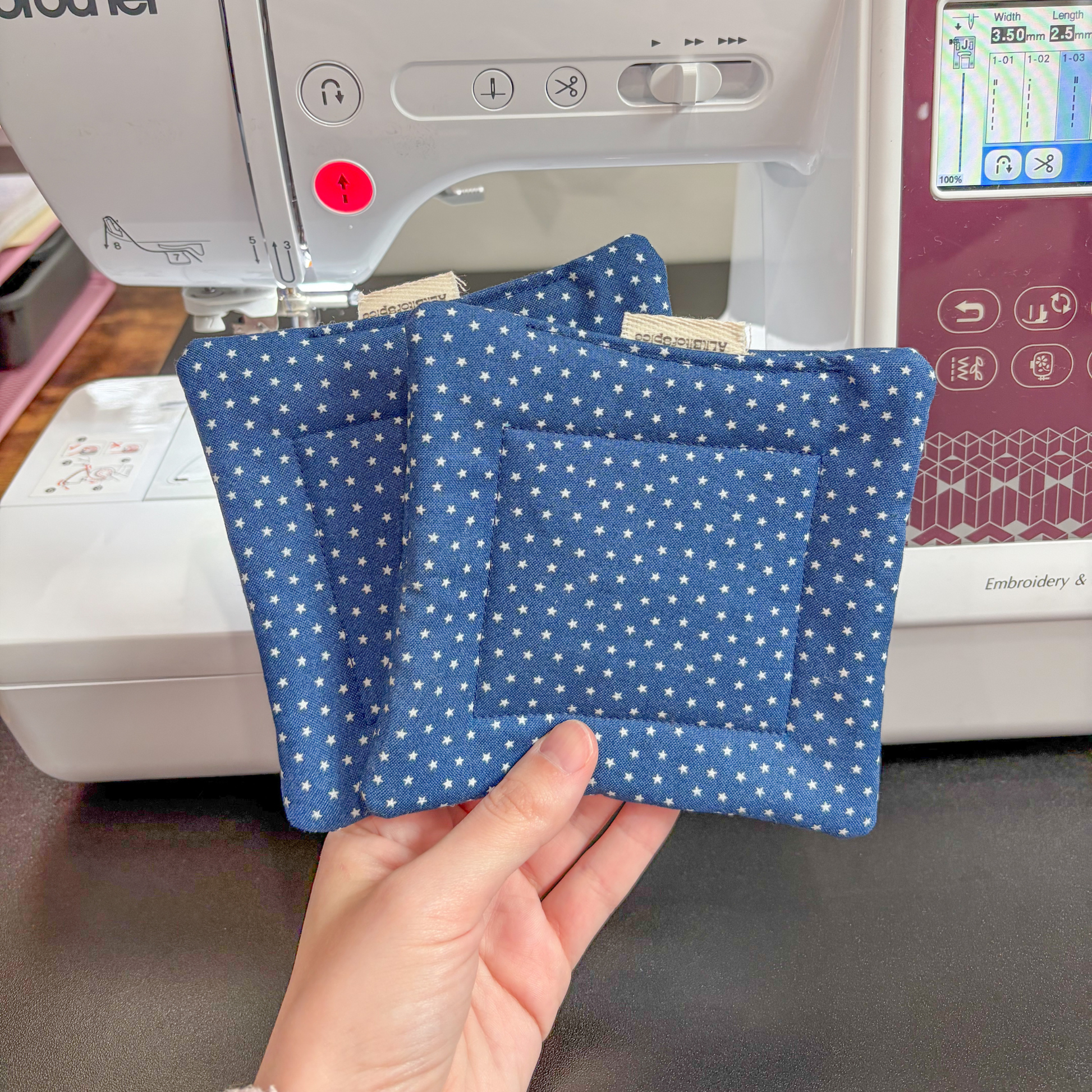 Two blue star pillow coasters held in front of a Brother sewing machine.
