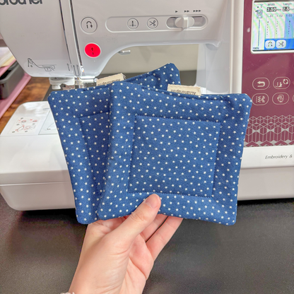 Two blue star pillow coasters held in front of a Brother sewing machine.
