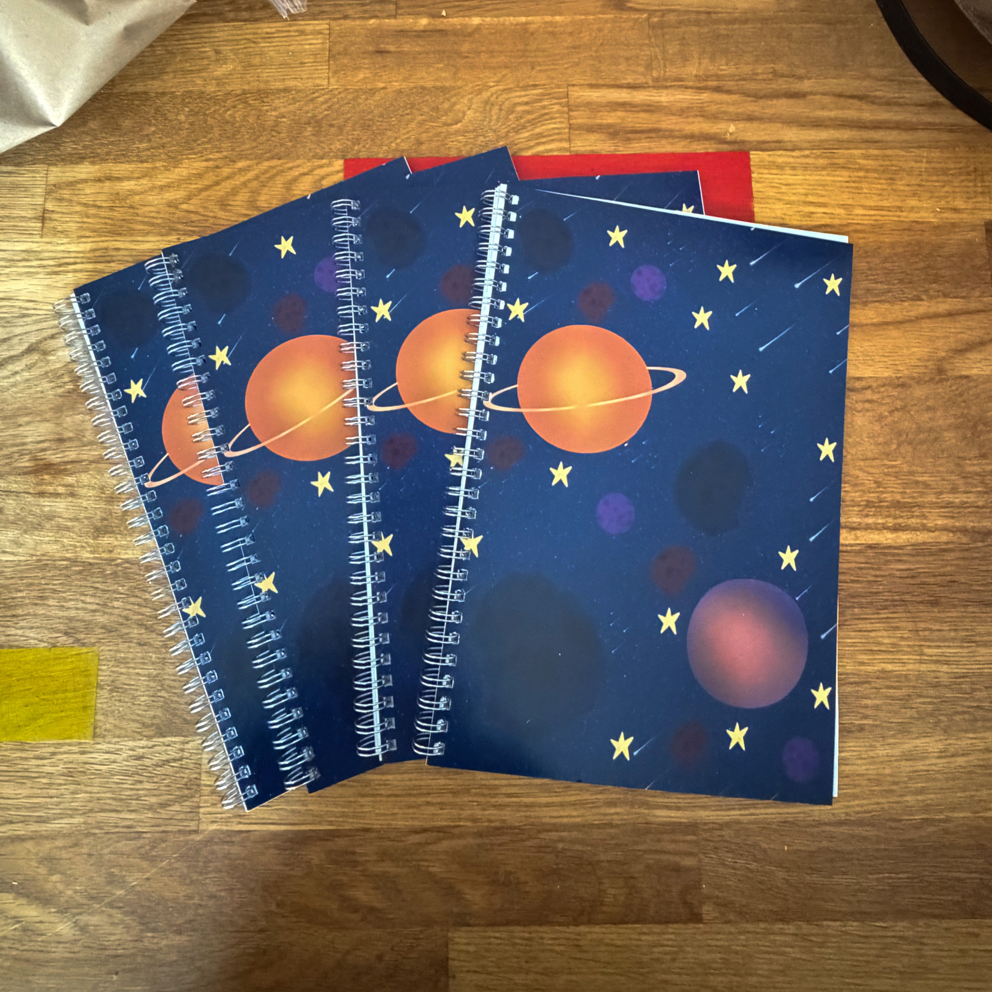 Three notebooks with space-themed covers on a wooden surface
