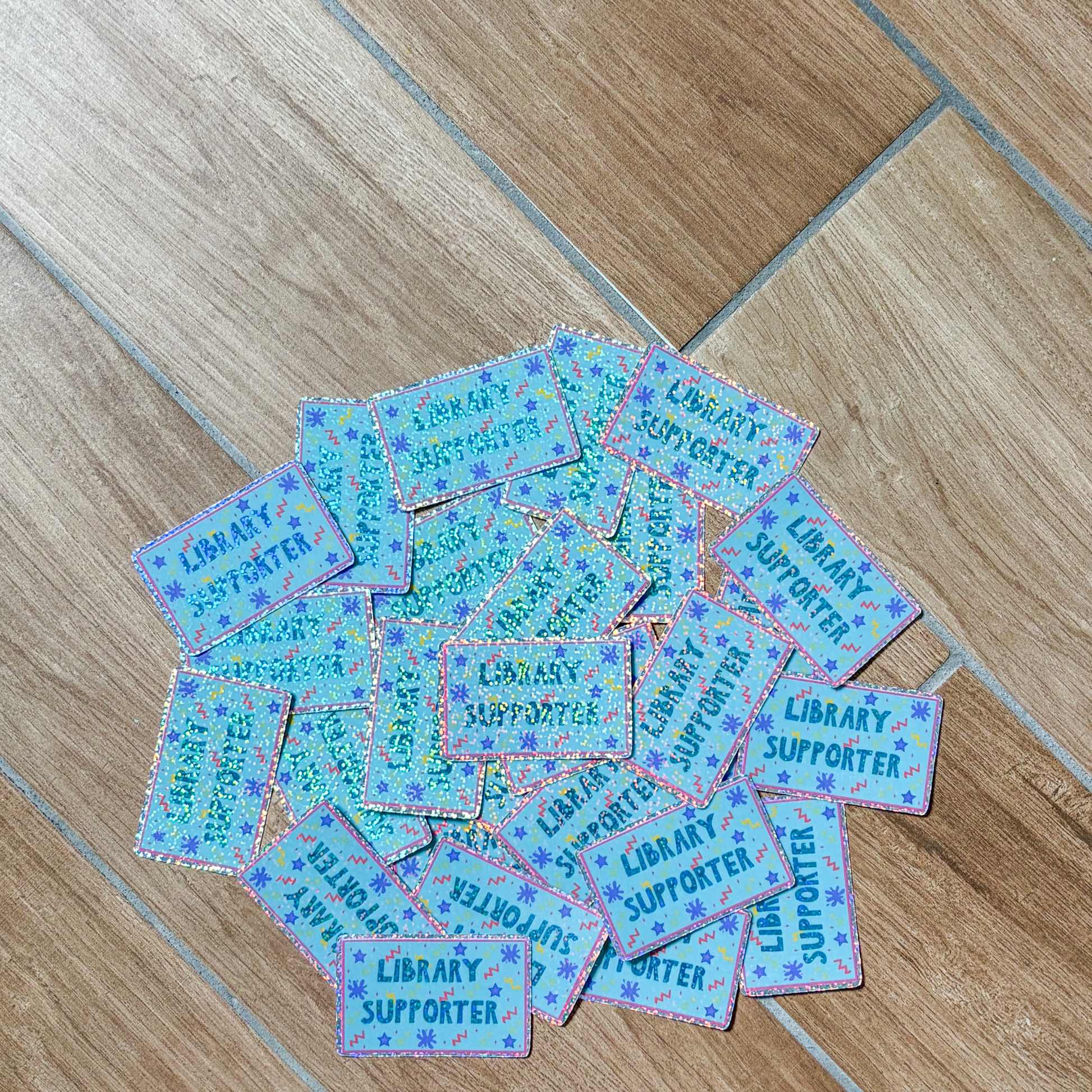 Collection of 'Library Supporter' stickers on a wooden floor