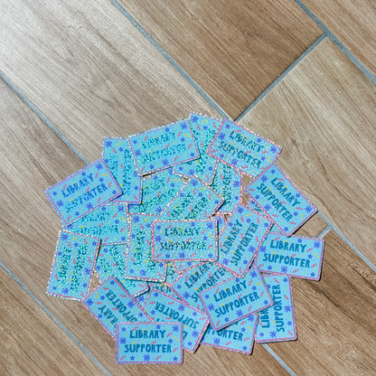Collection of 'Library Supporter' stickers on a wooden floor