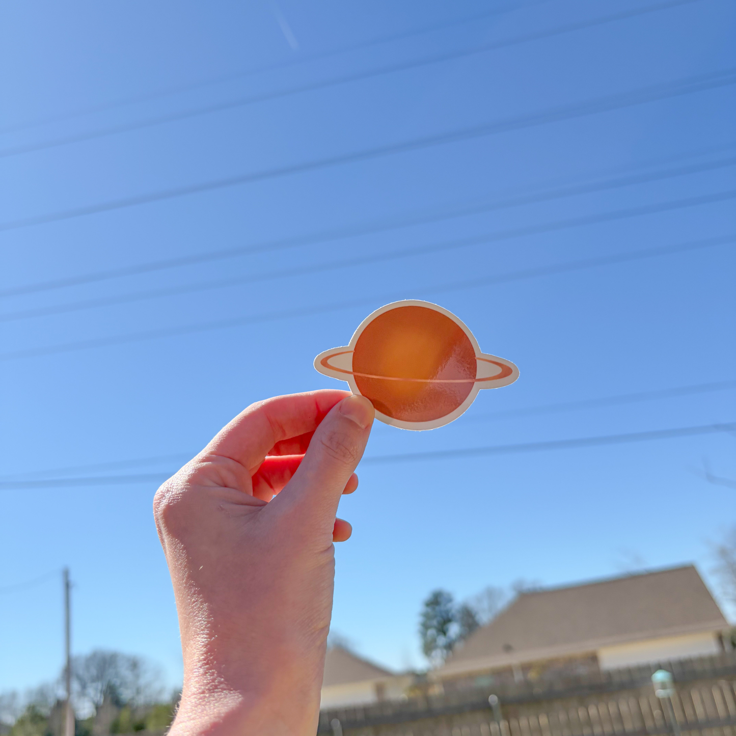 Hand holding a small plant-shaped sticker with a ring against a blue sky.