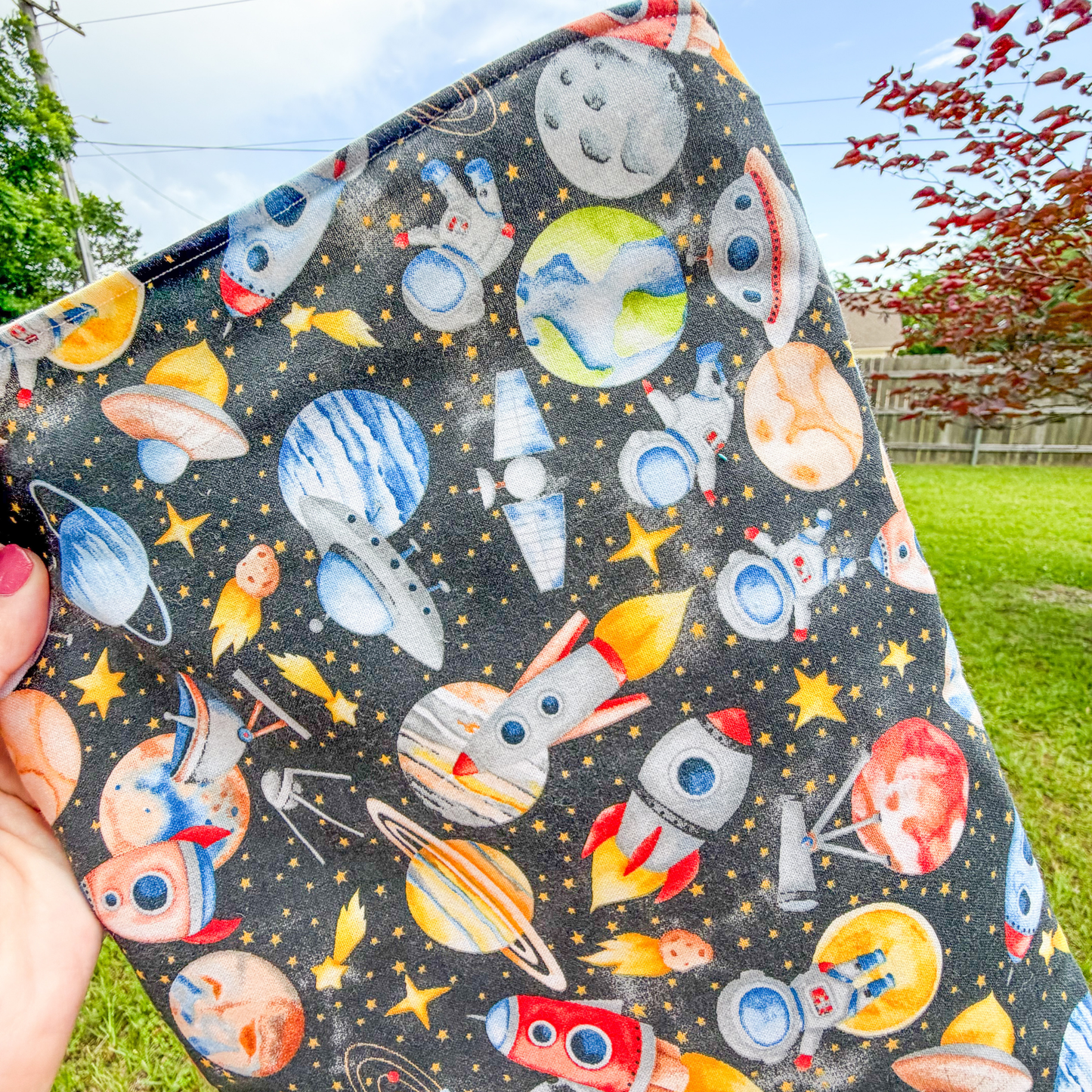 Space-themed pouch held outdoors with trees and grass in the background