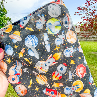 Space-themed pouch held outdoors with trees and grass in the background
