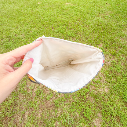 Hand holding open a book sleeve to reveal the light colored interior fabric against a grassy background