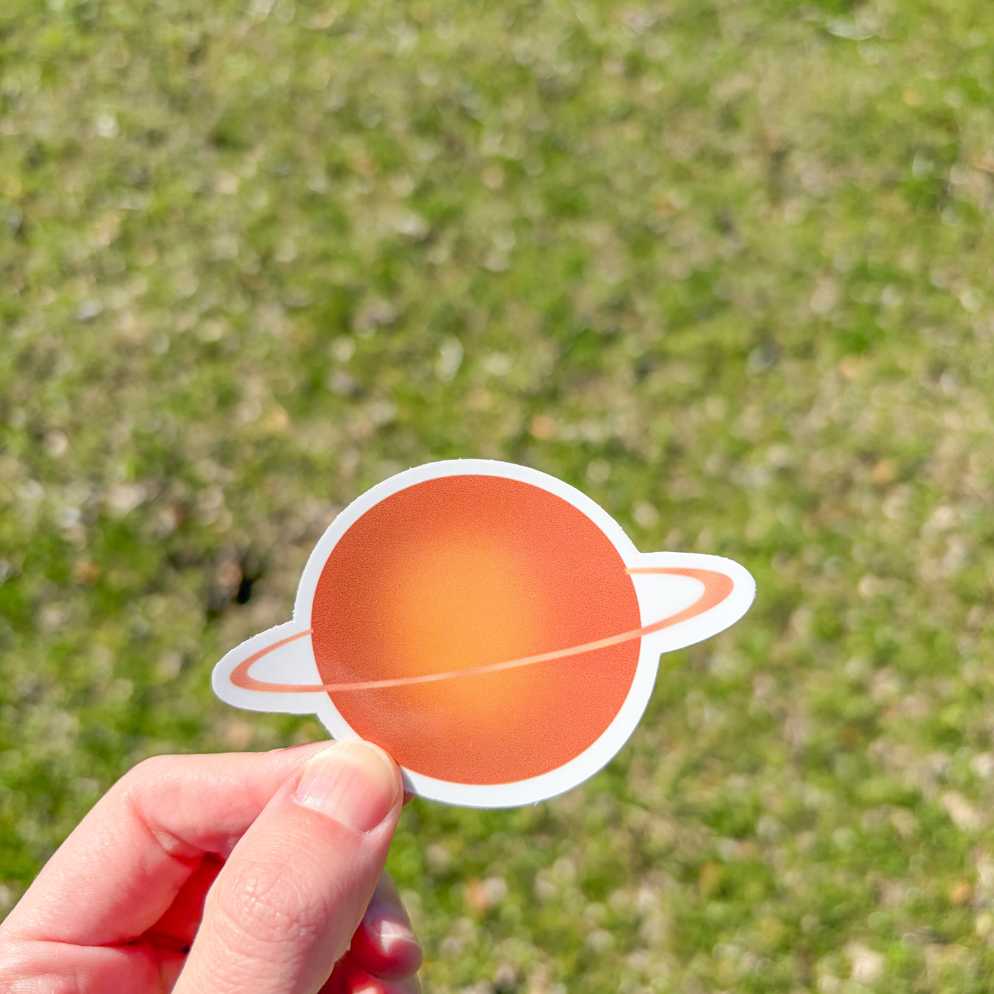 Hand holding a planet-shaped sticker against a grassy background