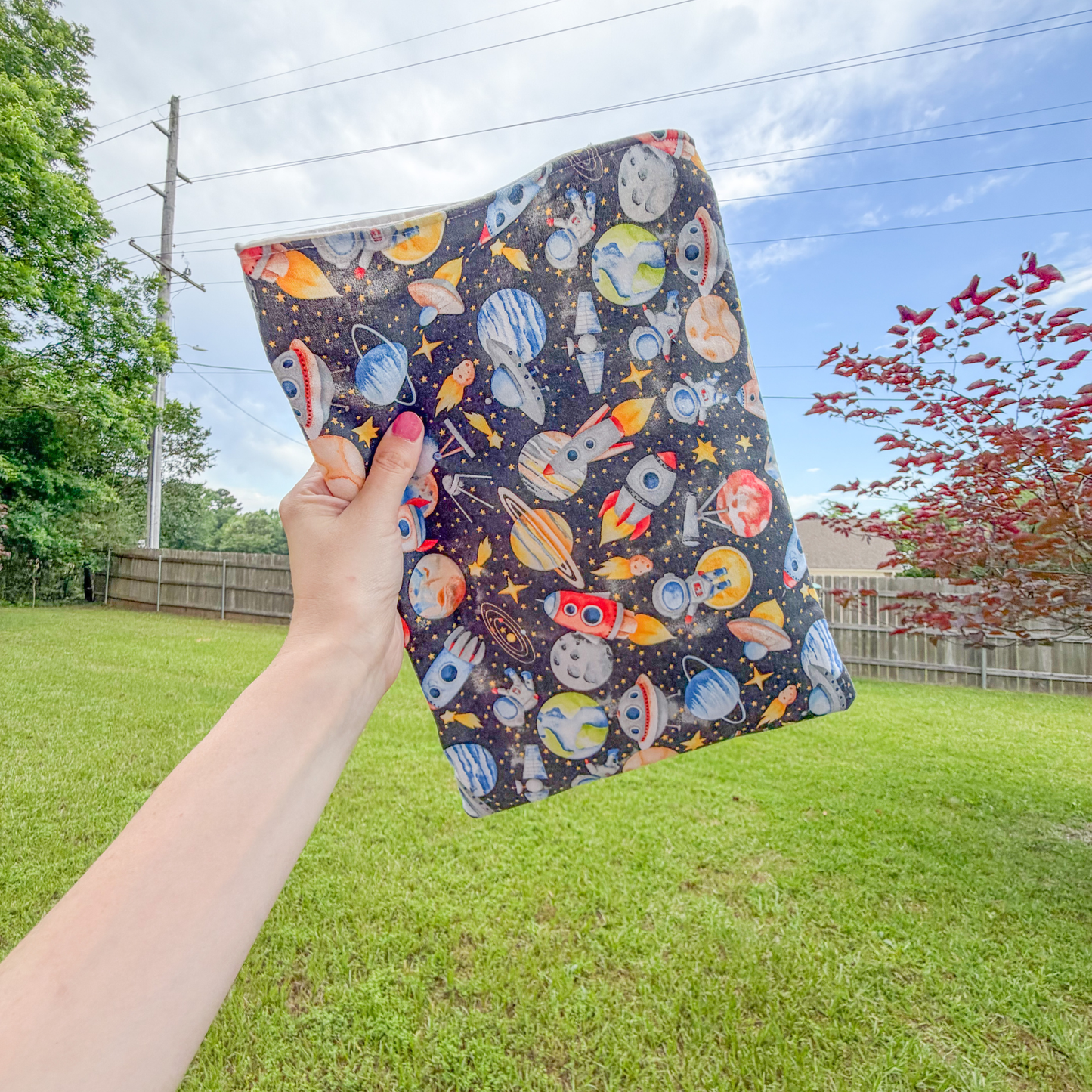 Hand holding a colorful book sleeve with space-themed design outdoors.