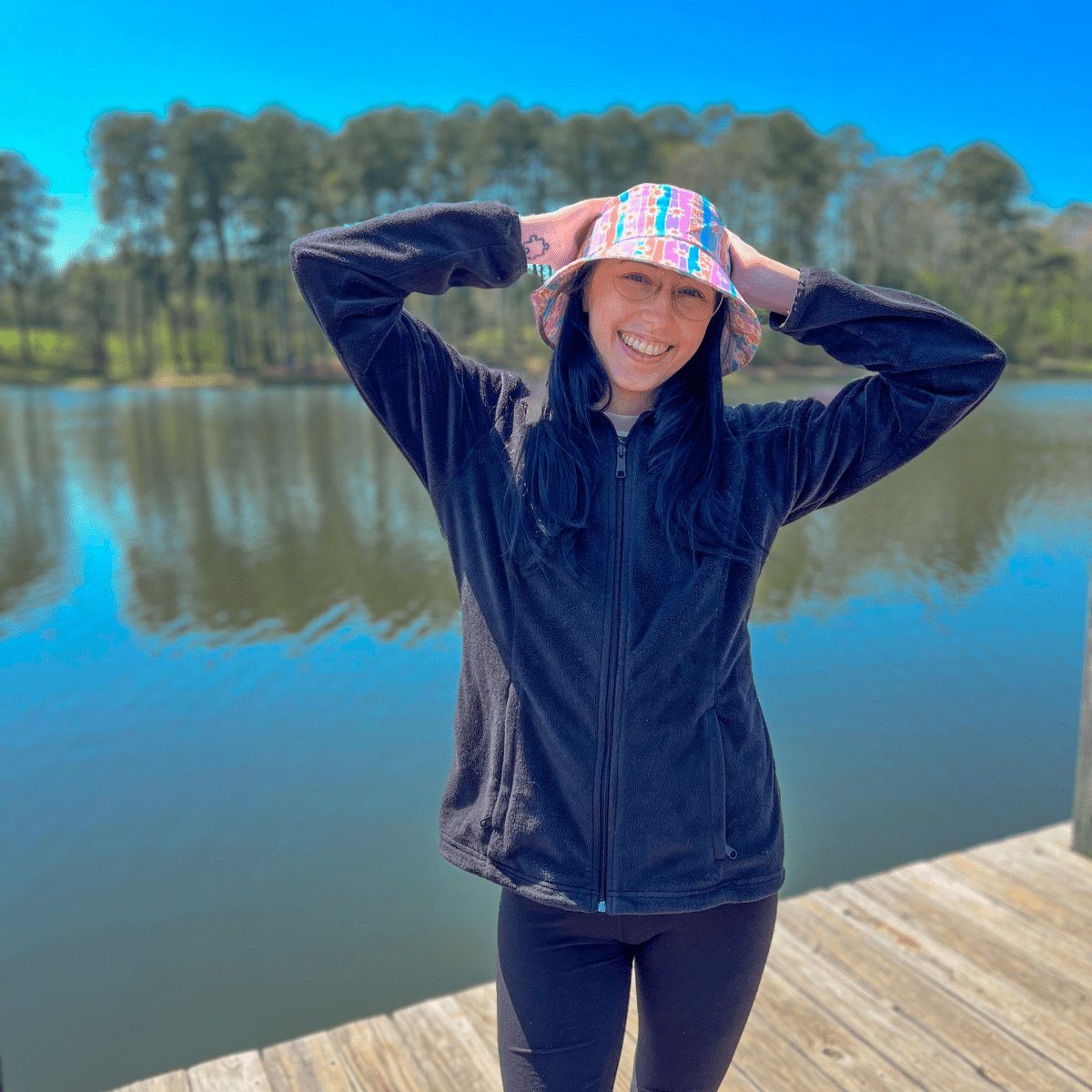 A person standing on a dock wearing a multicolored bucket hat with daisy and striped patterns.
