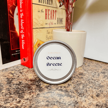 A candle tin labeled 'Ocean Breeze' placed on a kitchen counter with a book and a vase in the background.